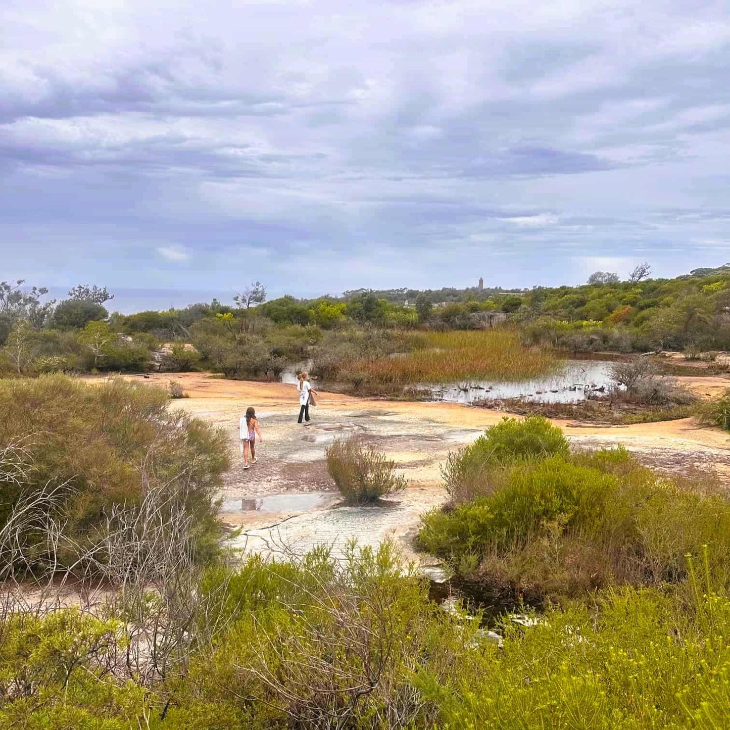 Two people standing on a rocky outcrop in a natural landscape with trees and a lake at North Head, in Manly Beach on Sydney's Northern Beaches.