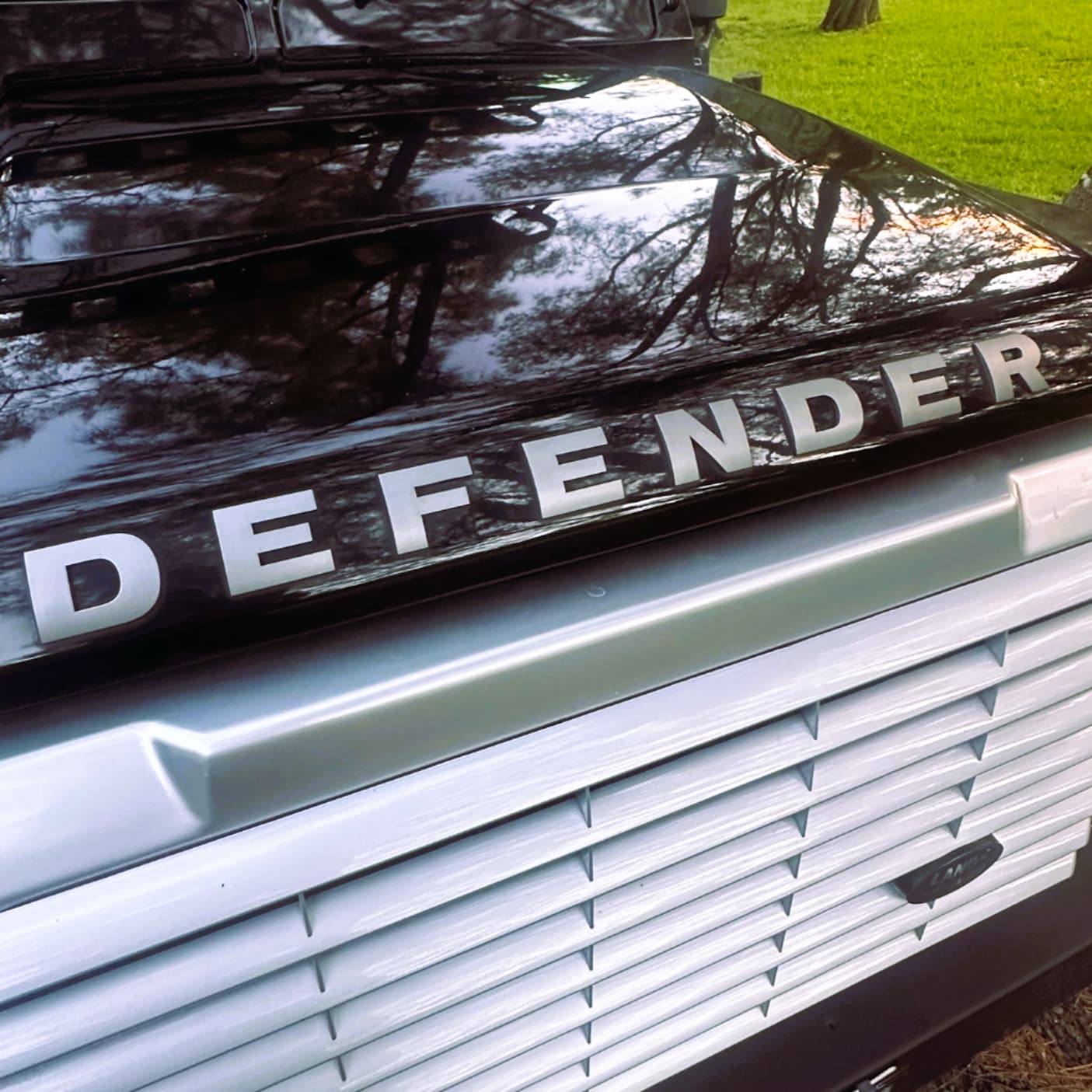 Close-up of the Salt and Trails Land Rover Defender with 'DEFENDER' branding on the grille.