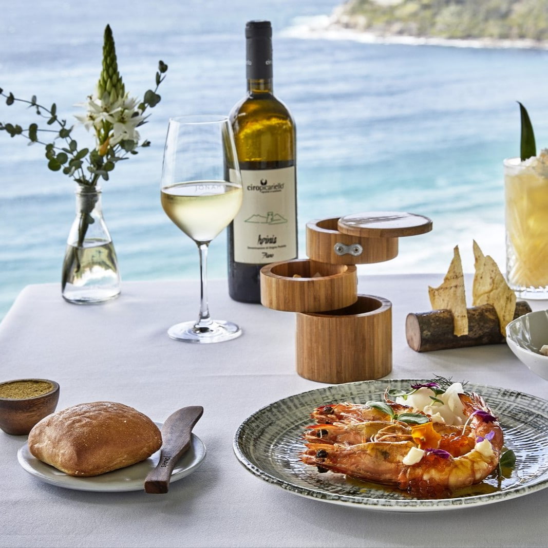 Table setting with shrimp dish, wine, bread, and flowers at Pilu Restaurant in Freshwater on Sydney Northern Beaches