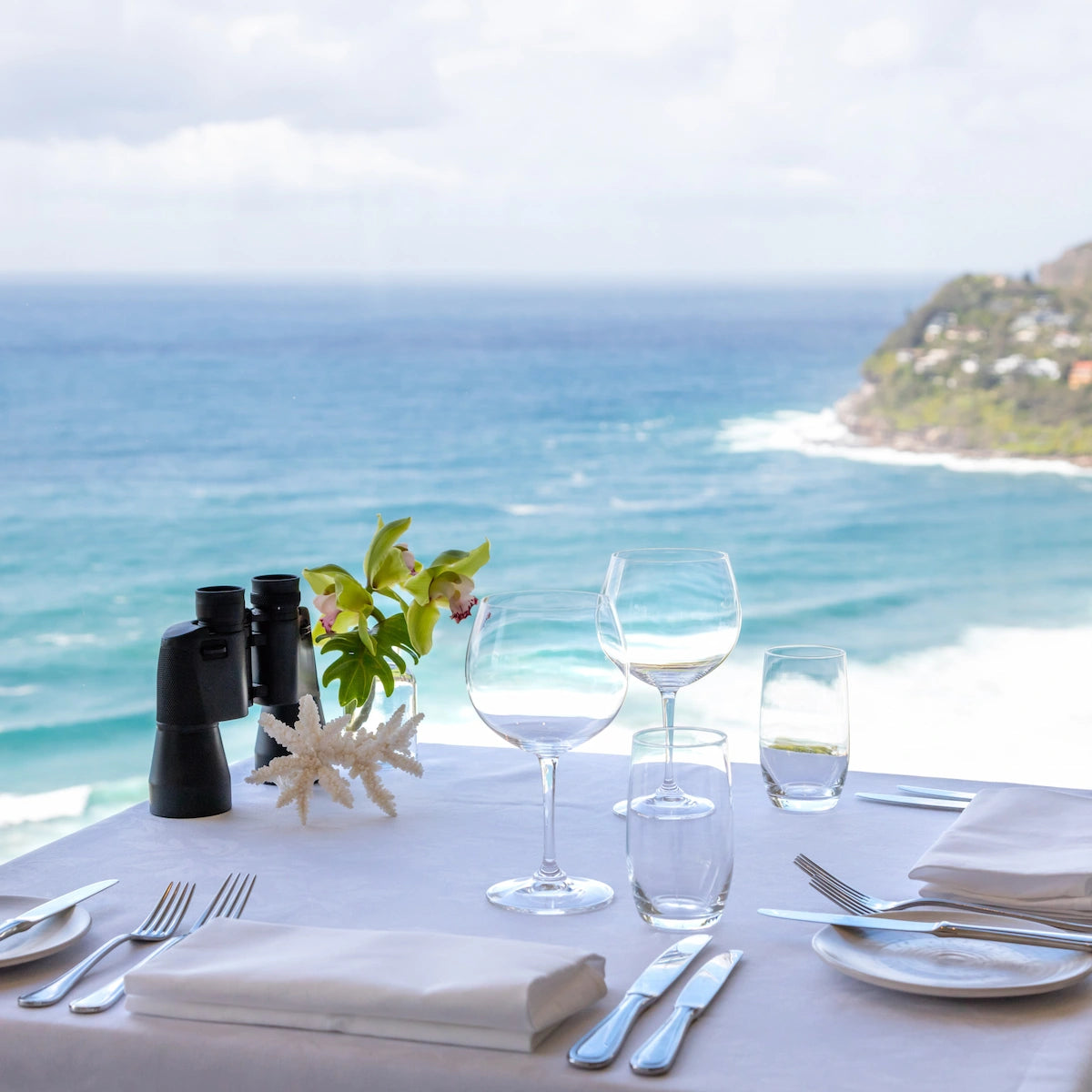 Dining table set with wine glasses, cutlery, and binoculars by the ocean at Jonah's restaurant at Whale Beach on Sydney's Northern Beaches.