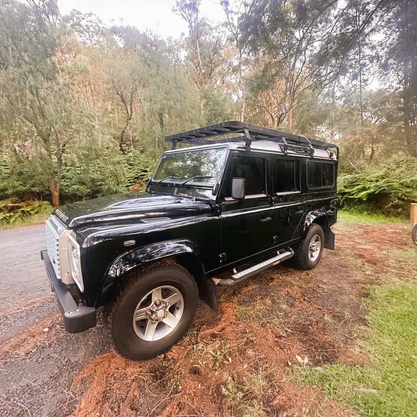 Salt and Trails black classic Land Rover Defender with a roof rack parked on a dirt road surrounded by trees in Narrabeen, on Sydney's Northern Beaches.