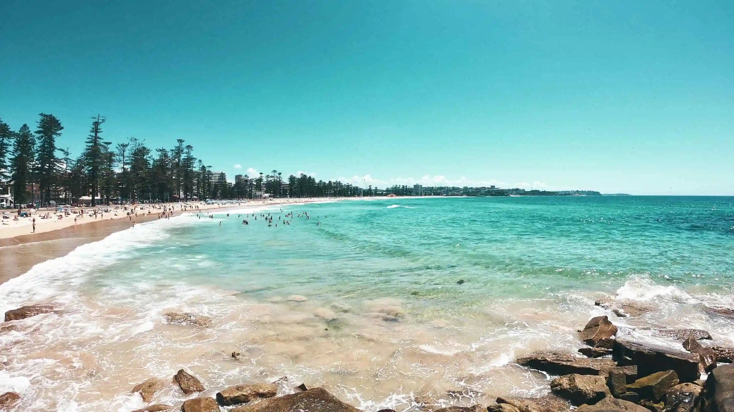 Beach scene with clear blue water and a bright sky at Manly Beach on Sydney's Northern Beaches