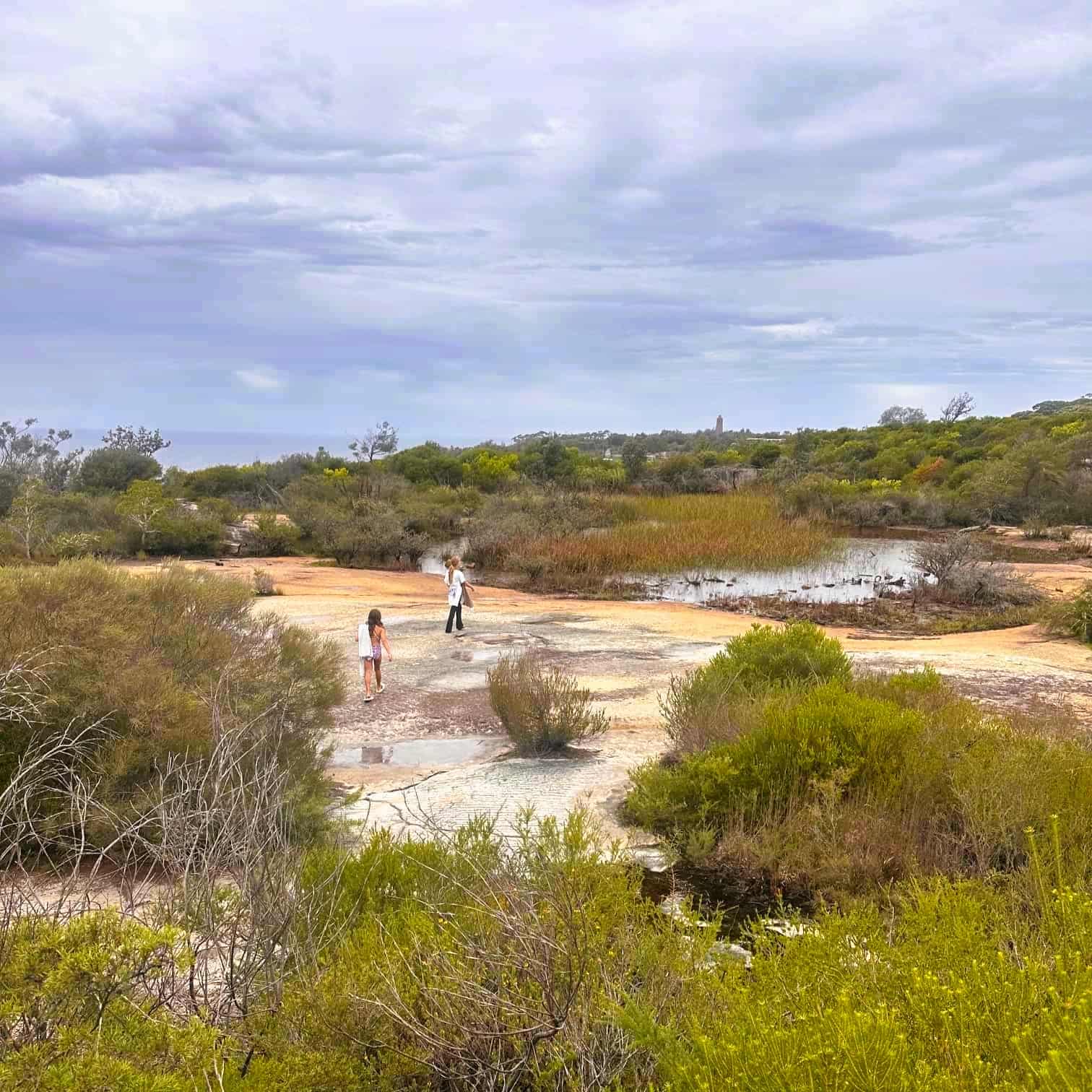 Two people standing on a rocky outcrop in a natural landscape with trees and a lake at North Head, in Manly Beach on Sydney's Northern Beaches.