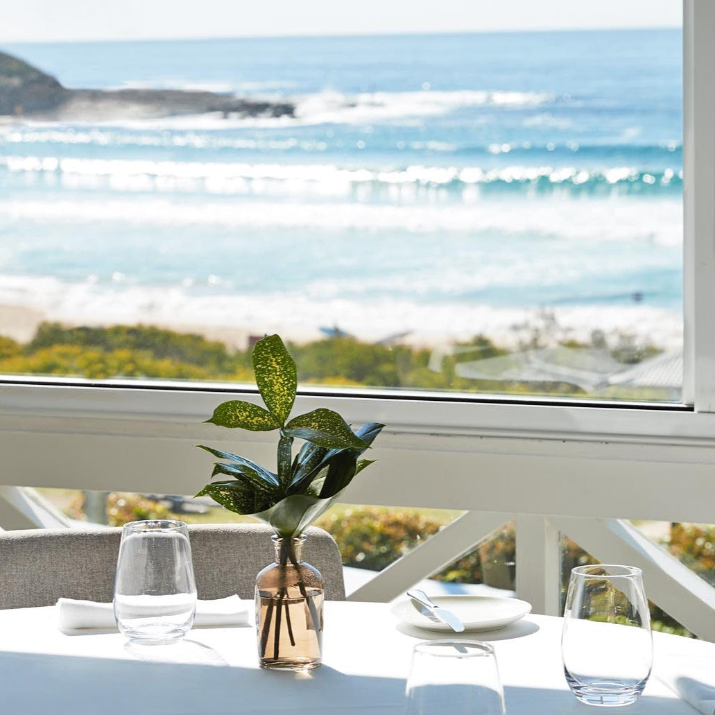Table setting with a vase of leaves by a window with a scenic view of the ocean from Pilu Restaurant in Freshwater on Sydney Northern Beaches