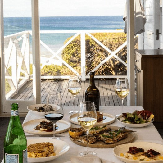 Table set with food and wine by a window with an ocean view from Pilu restaurant at Freshwater on Sydney Northern Beaches