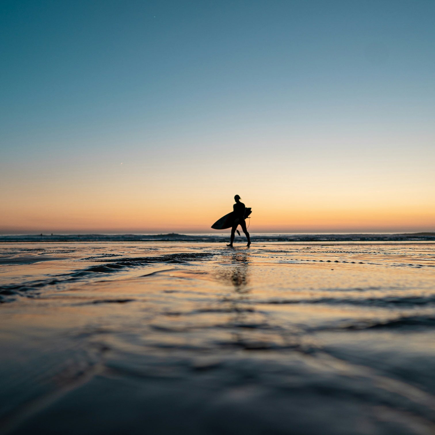 Person walking on a beach with a surfboard at sunrise in Manly Beach on Sydney's Northern Beaches.